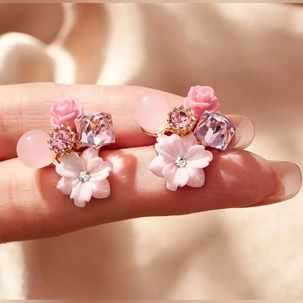 Pair of pink floral earrings with gemstones on a hand against a soft background