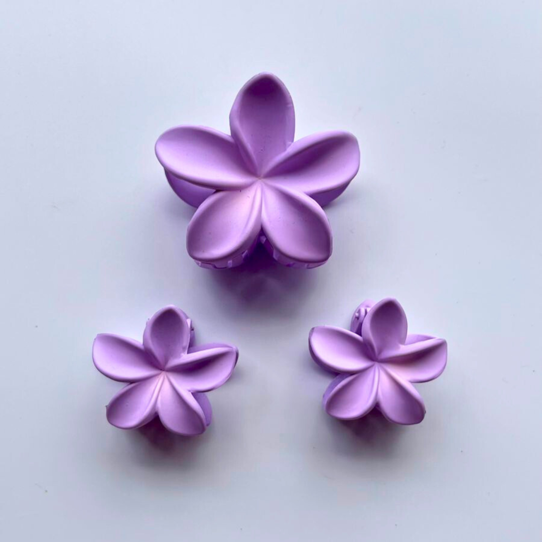 Three purple flower-shaped claw clips on a light grey background