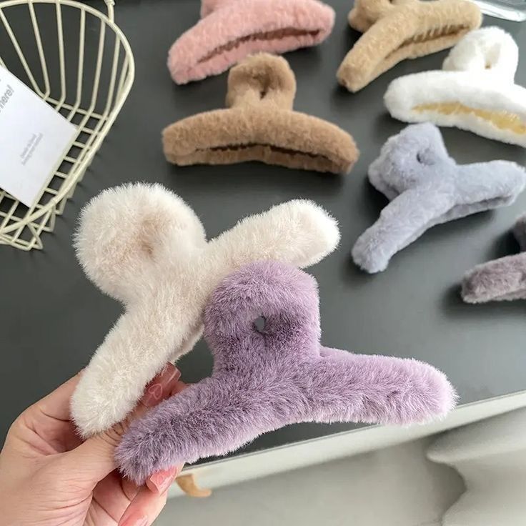 Fluffy hair clips in various colours on a dark surface with a hand holding a purple one.