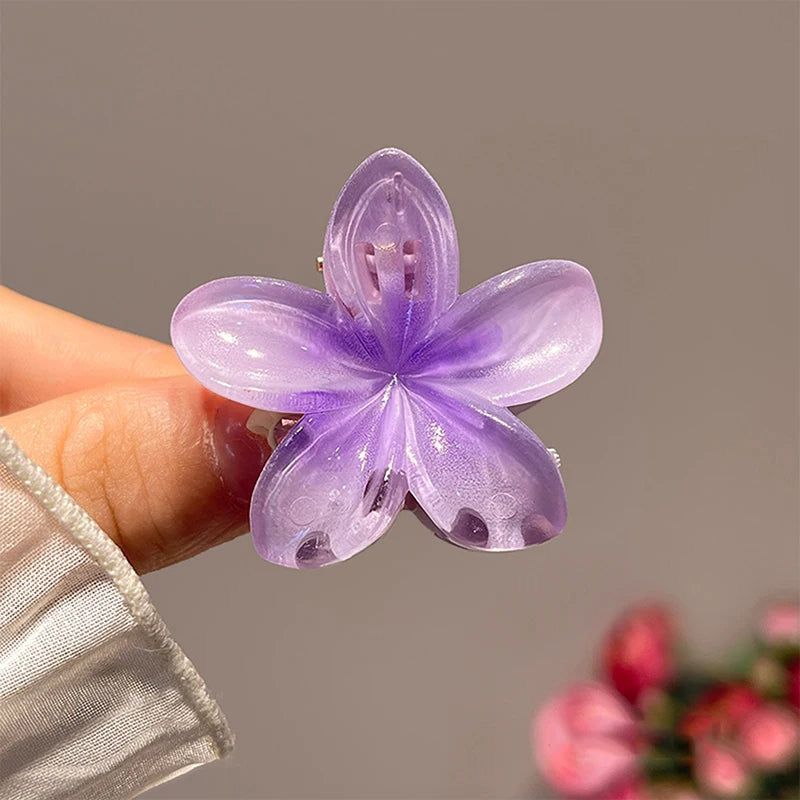 Purple flower-shaped hair clip held by a hand against a neutral background