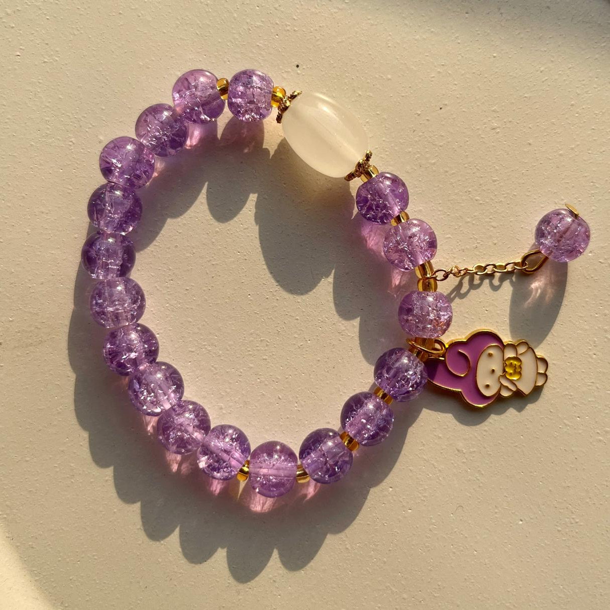 Purple beaded bracelet with a Hello Kitty charm on a beige background