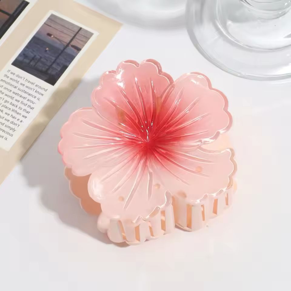Pink flower-shaped hair clip on a white surface with a book and glass in the background