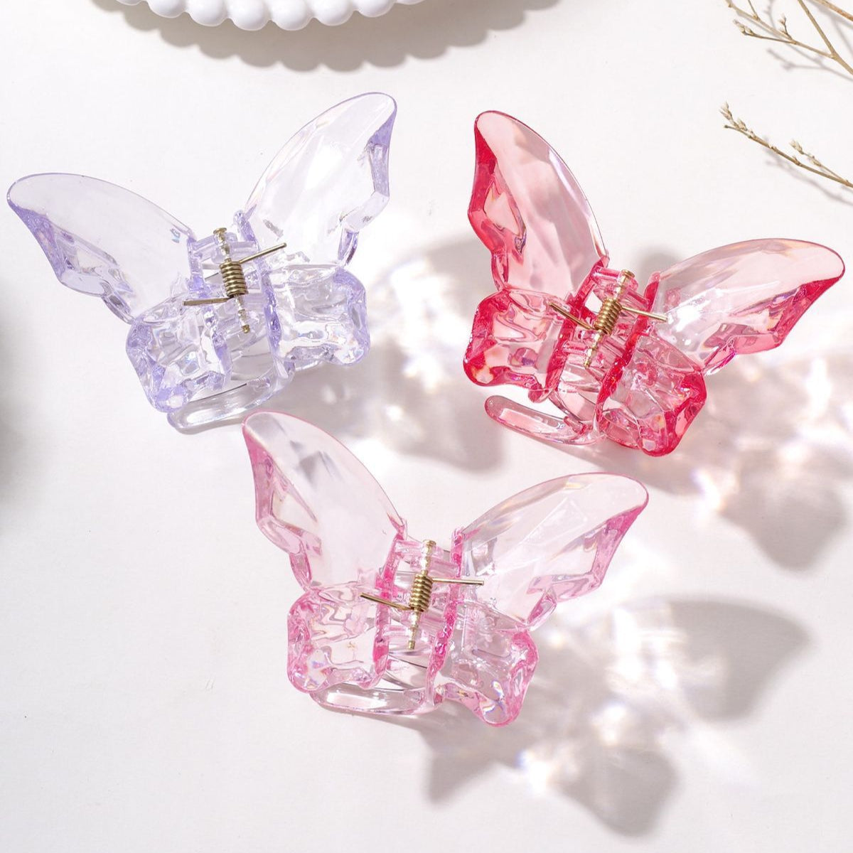 Three butterfly-shaped hair clips in pink, clear, and red on a white surface.