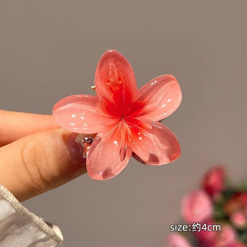 Pink flower-shaped hair clip held by a hand with a blurred background