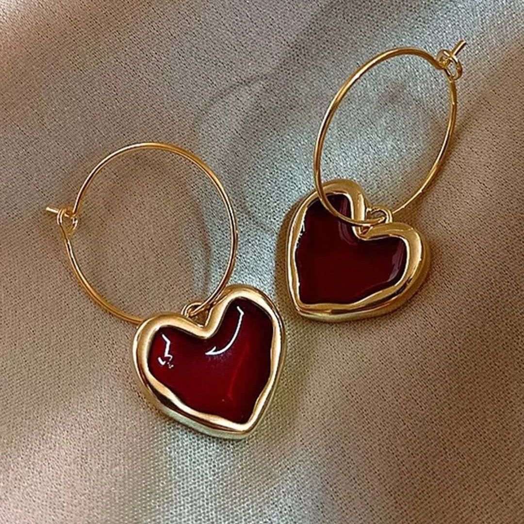 Gold hoop earrings with red heart charms on a beige background