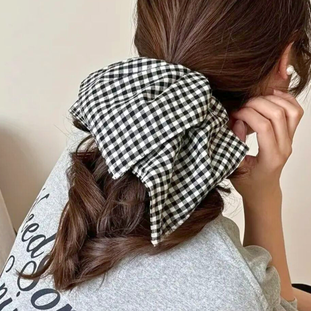 Person with a checkered square shaped scrunchie or hair tie adjusting their hair against a neutral background