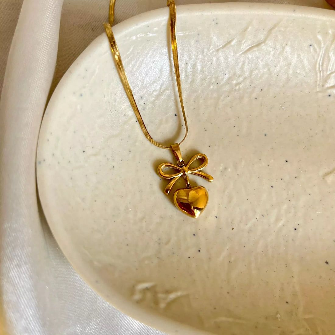 Gold necklace with a heart and bow pendant on a textured white surface