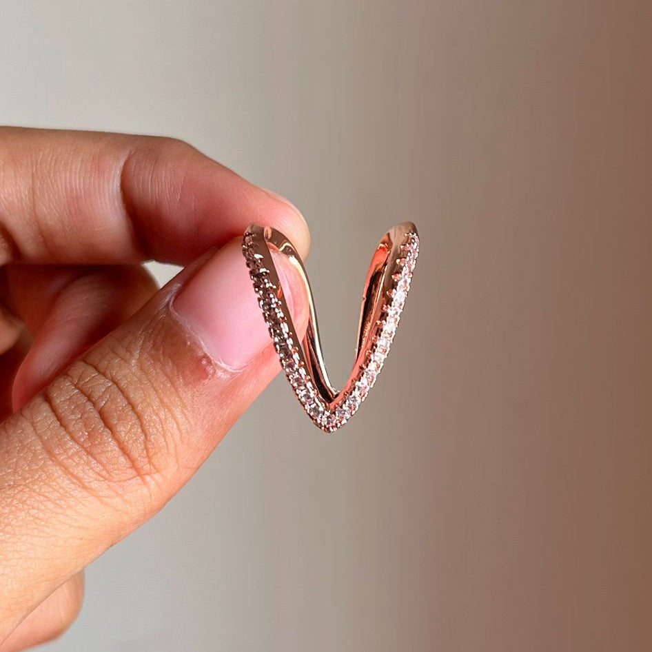Rose gold ring held by a hand against a neutral background