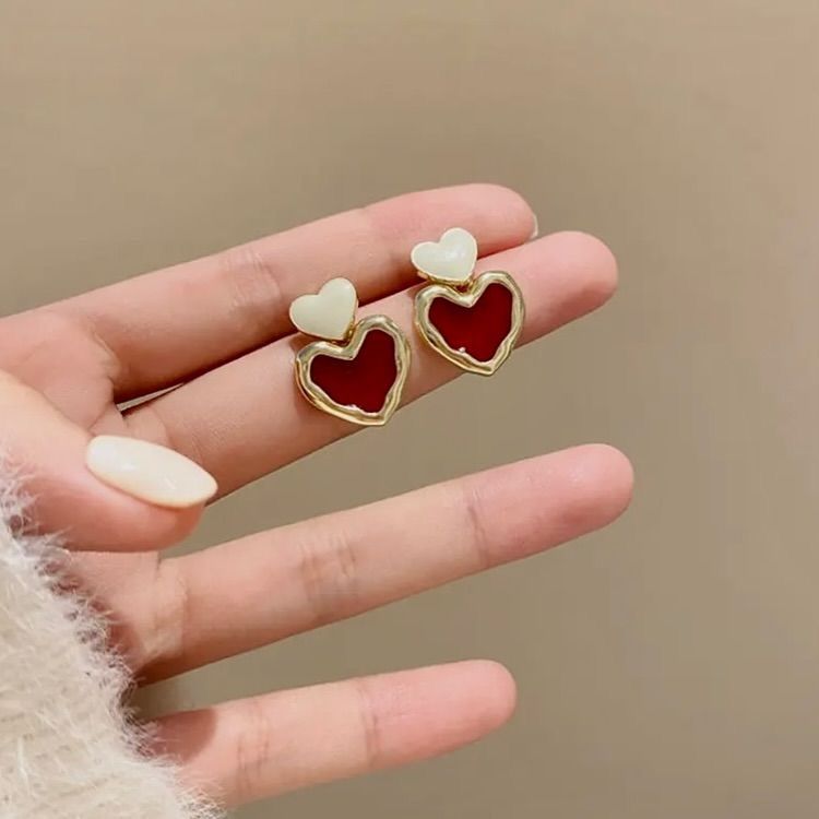 Heart-shaped earrings held between fingers against a beige background