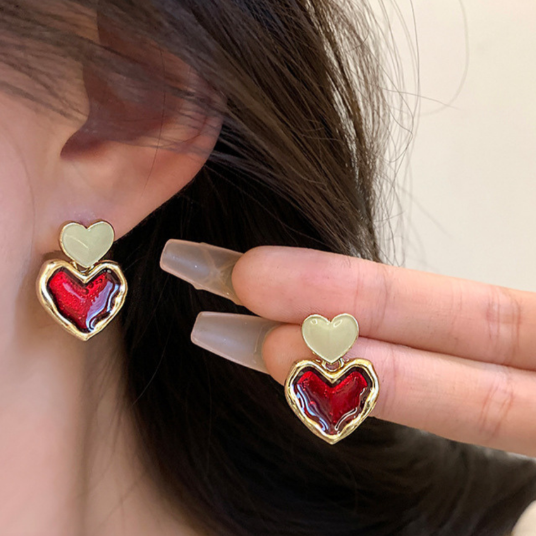 Heart-shaped earrings with red and gold design worn by a person