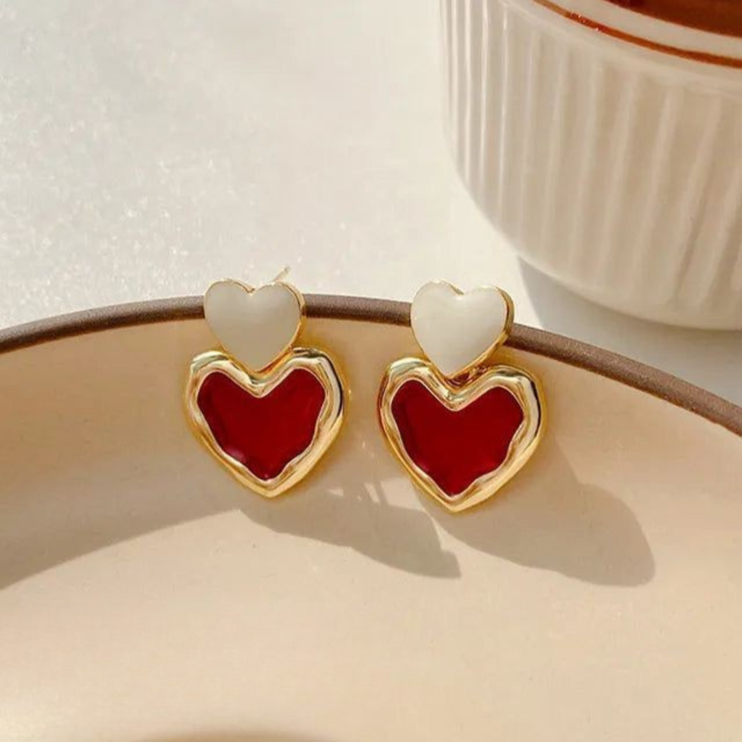 Heart-shaped earrings with red and gold design on a beige surface.