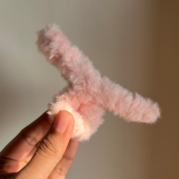 Pink fuzzy Hair Clips held by a hand against a neutral background