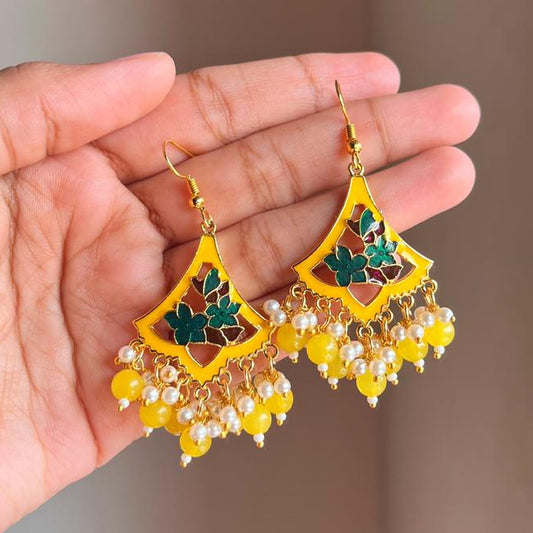 Yellow earrings with green accents held by a hand against a neutral background
