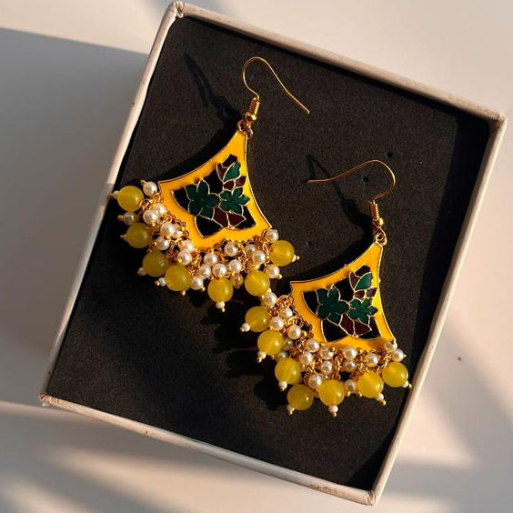 Gold earrings with green and yellow stones in a box on a light background