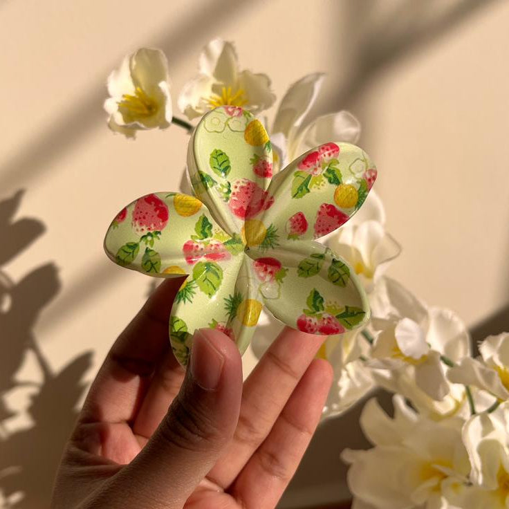 Hand holding a decorative flower-shaped hair clip with floral patterns against a neutral background