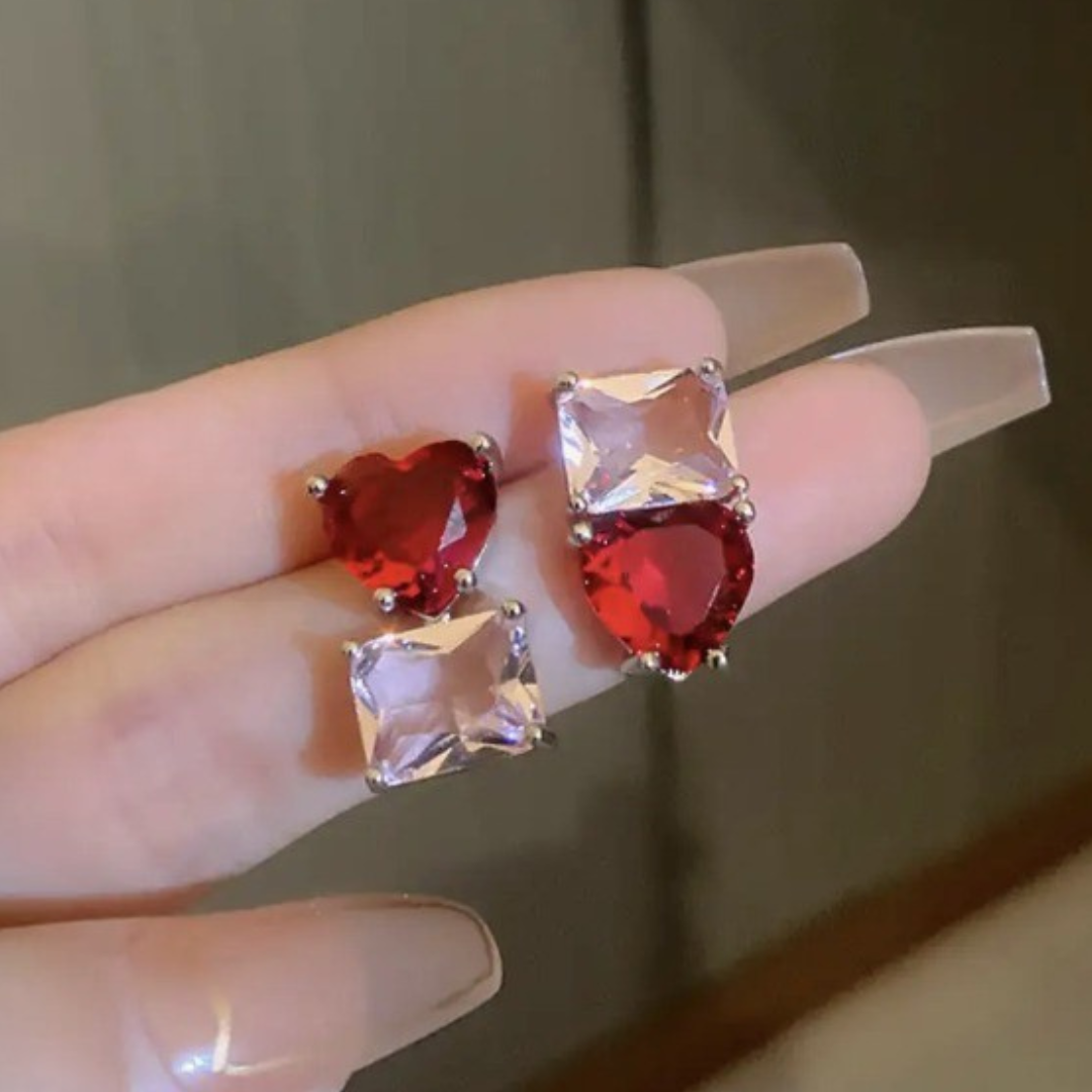 Heart-shaped and square-cut gemstone earrings on a hand with a neutral background