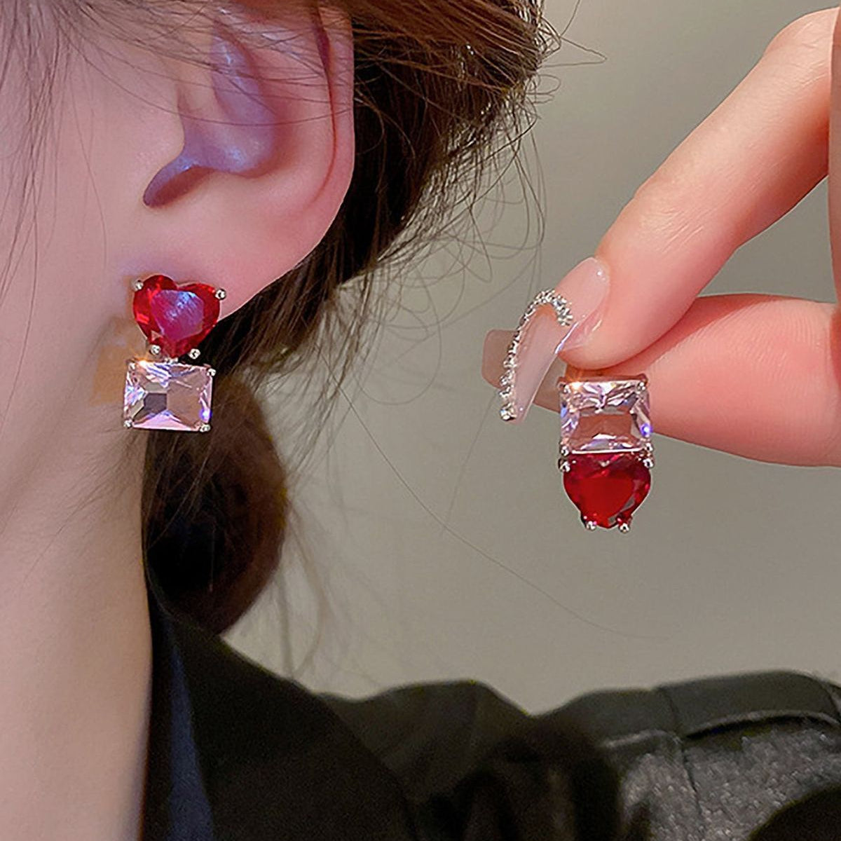 Close-up of a person wearing red and clear gemstone earrings with a neutral background.
