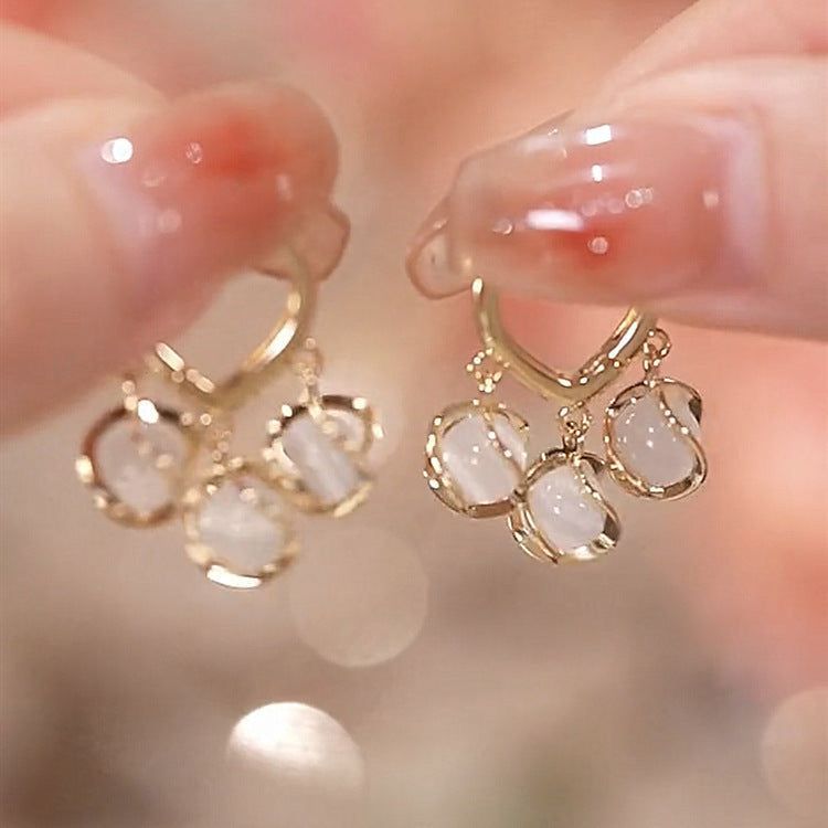 Gold hoop earrings with white stones held between fingers against a blurred background