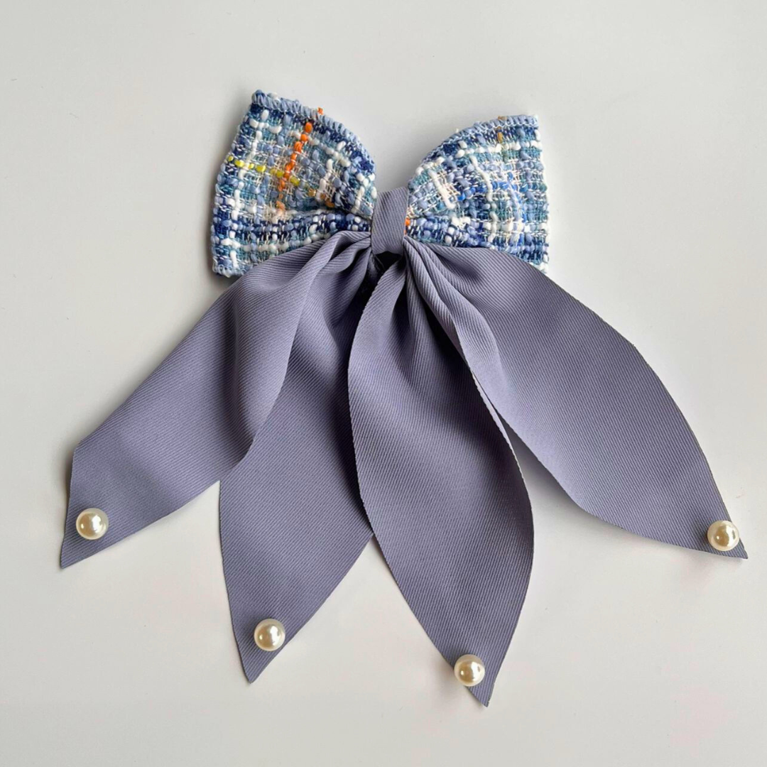 Hair bow with plaid top and solid purple ribbon on a light gray background