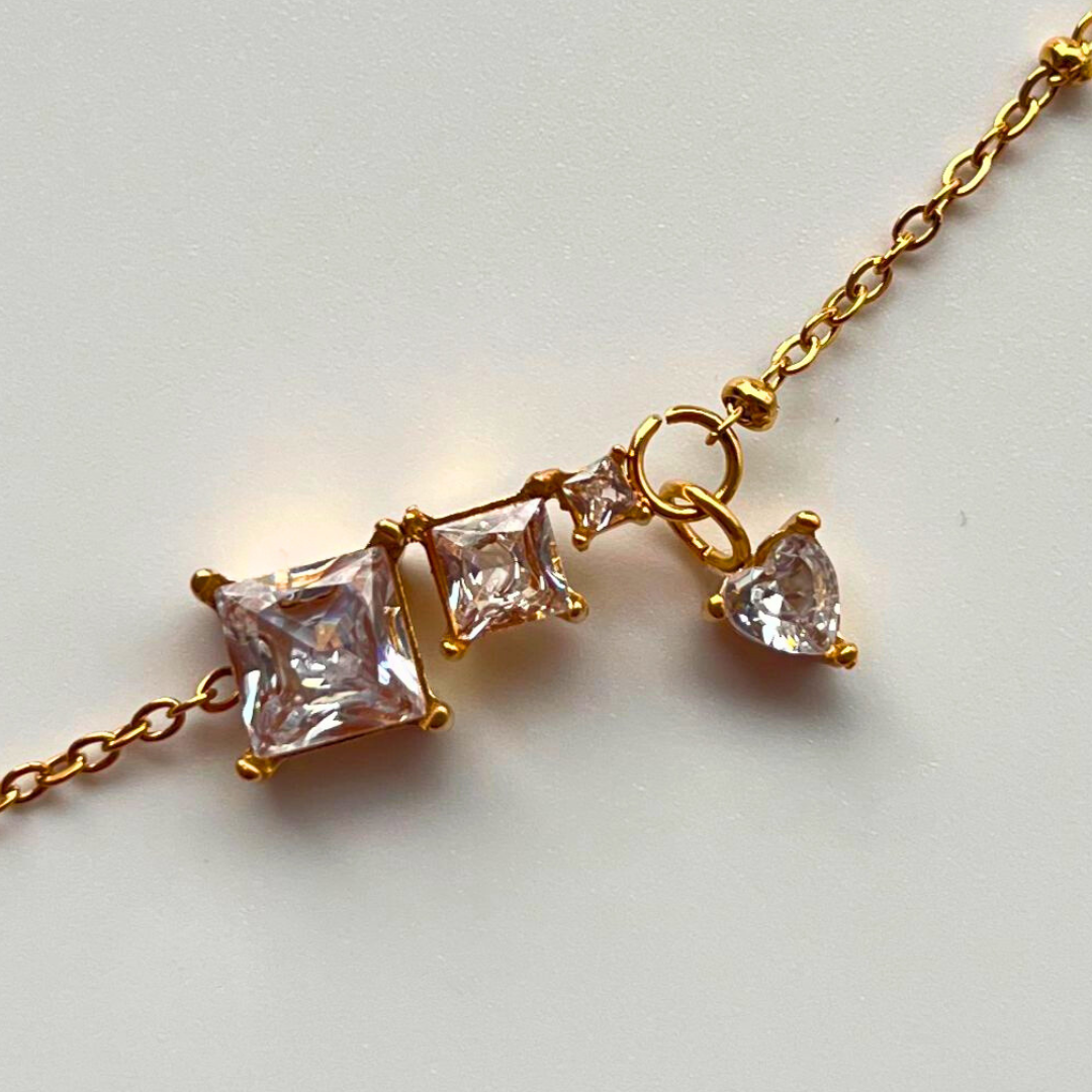 Gold bracelet with three clear gemstones on a light gray background