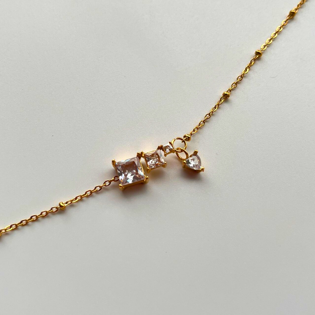 Gold bracelet with three diamond-like stones on a light gray background