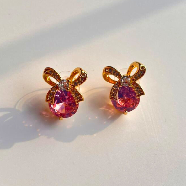Pair of bow-shaped earrings with pink gemstones on a light background