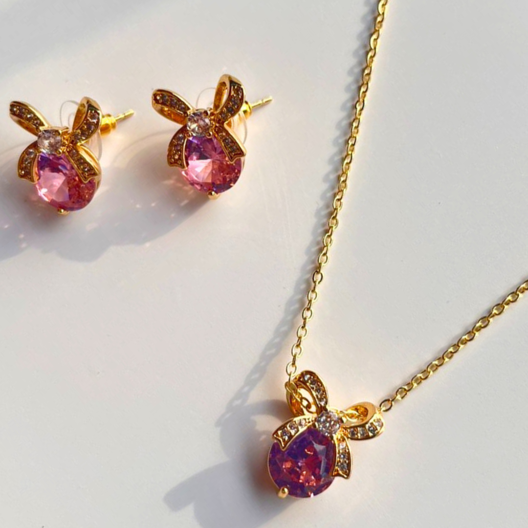 Gold necklace with pink teardrop pendant and matching earrings on a white background