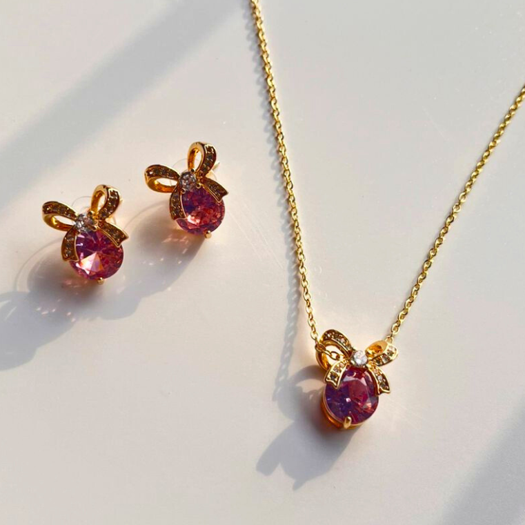 Gold necklace and earrings with pink gemstones on a light background