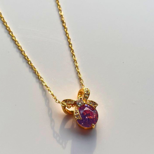 Gold necklace with a purple gemstone pendant on a light gray background