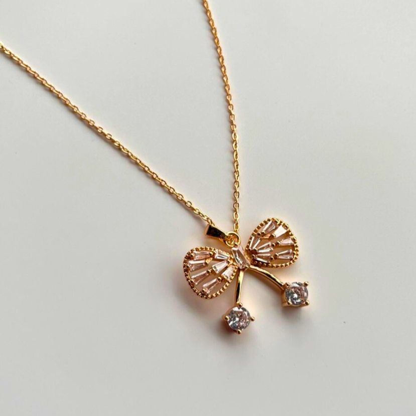 Gold bow-shaped necklace with diamond accents on a light gray background
