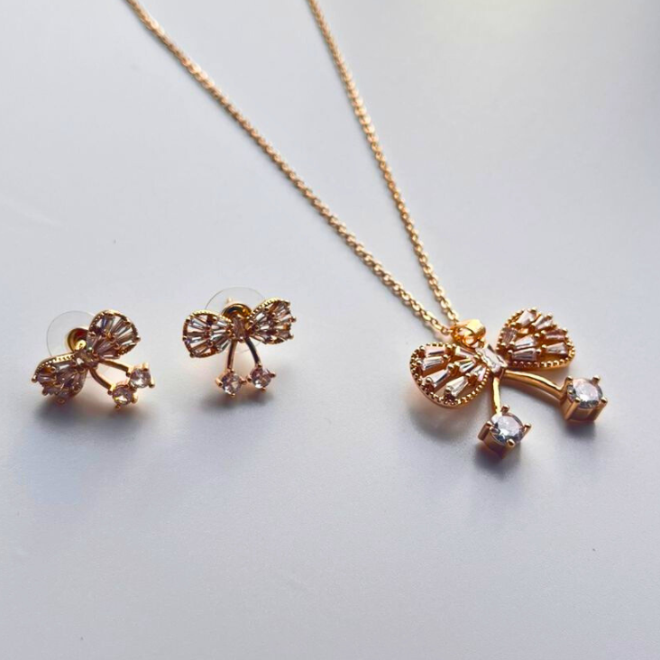 Gold bow-shaped necklace and earrings on a light gray background