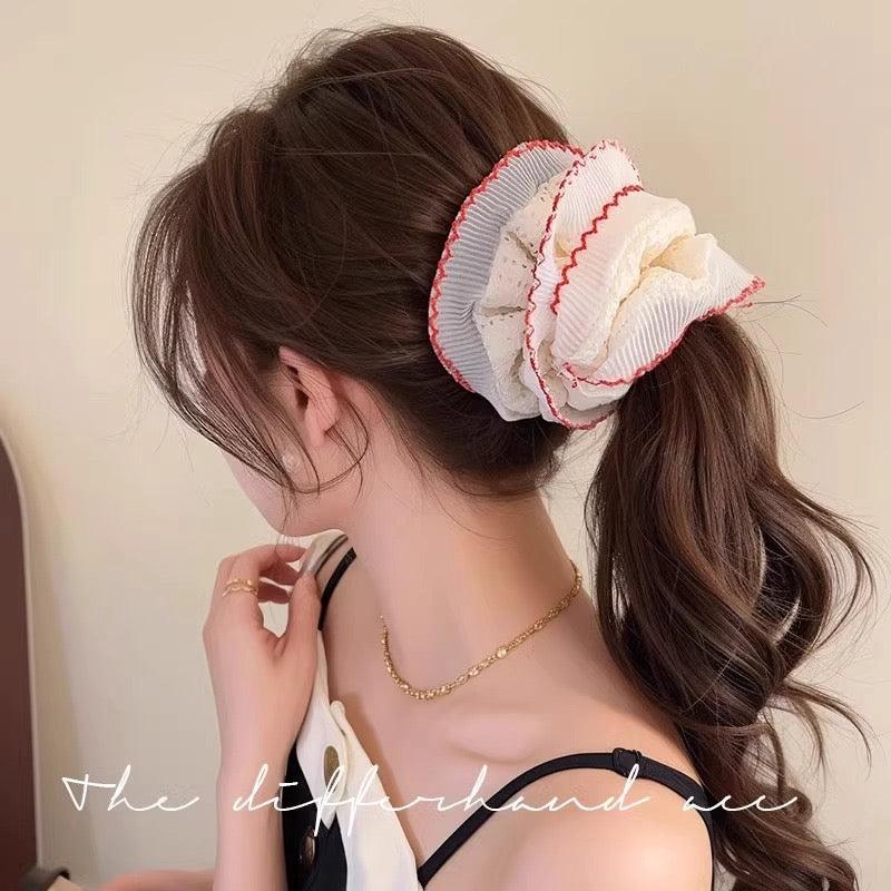 Woman with a decorative hair ruffle scrunchie in her hair against a neutral background