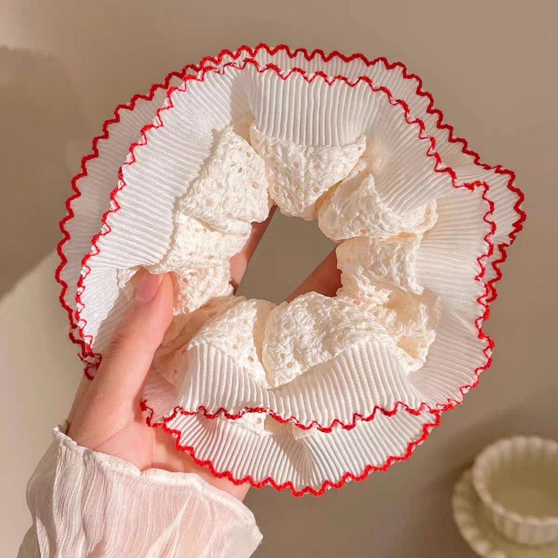 White lace scrunchie with red trim held by a hand against a neutral background