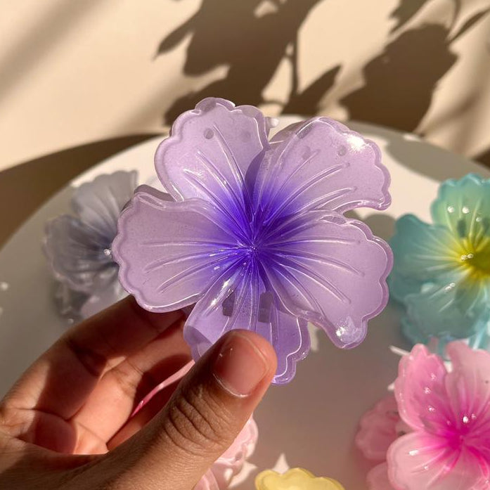 Hand holding a violet flower-shaped hair clip with other colorful flowers in the background