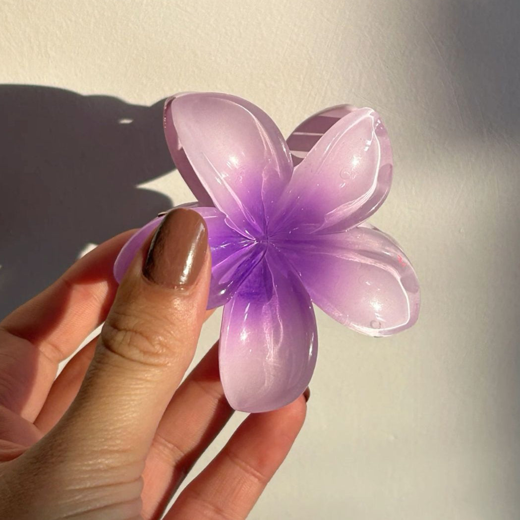 Hand holding a purple flower-shaped Viral Claw Clip against a neutral background