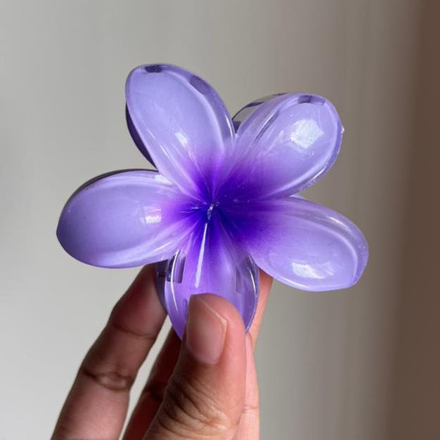 Hand holding a purple flower-shaped hair clip against a plain background