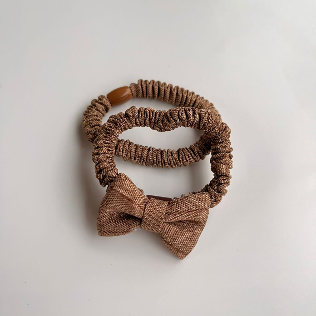 Brown hair scrunchie with a bow on a light gray background