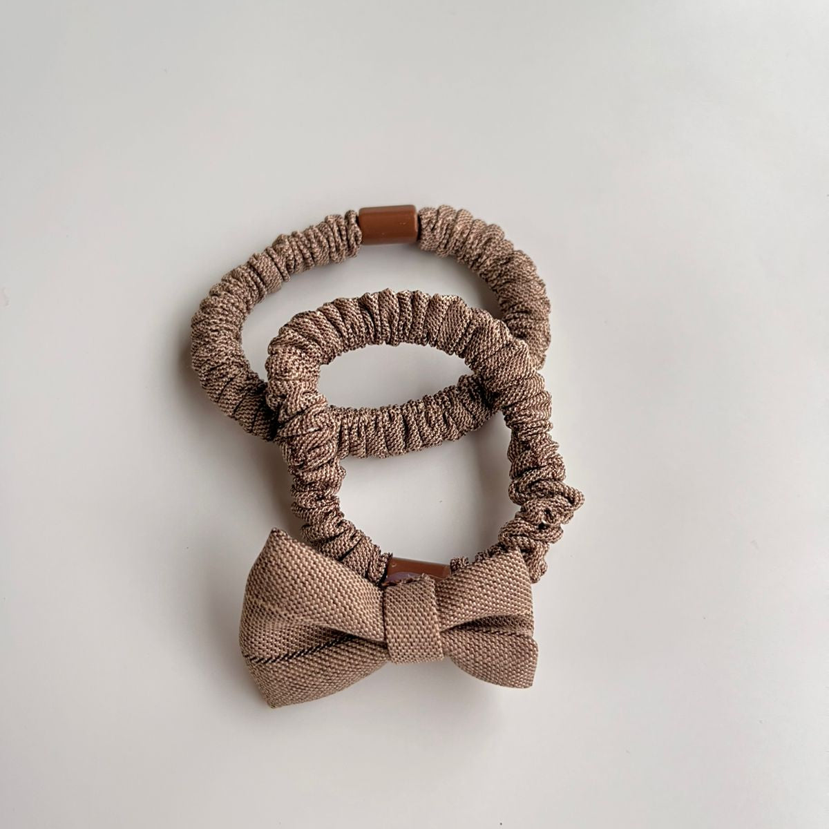 Two brown scrunchies with a bow on a light gray background