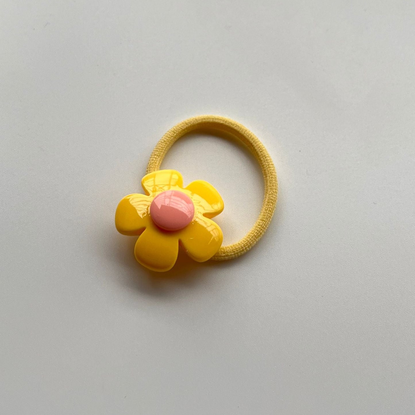 Yellow hair elastic with a pink center on a light gray background