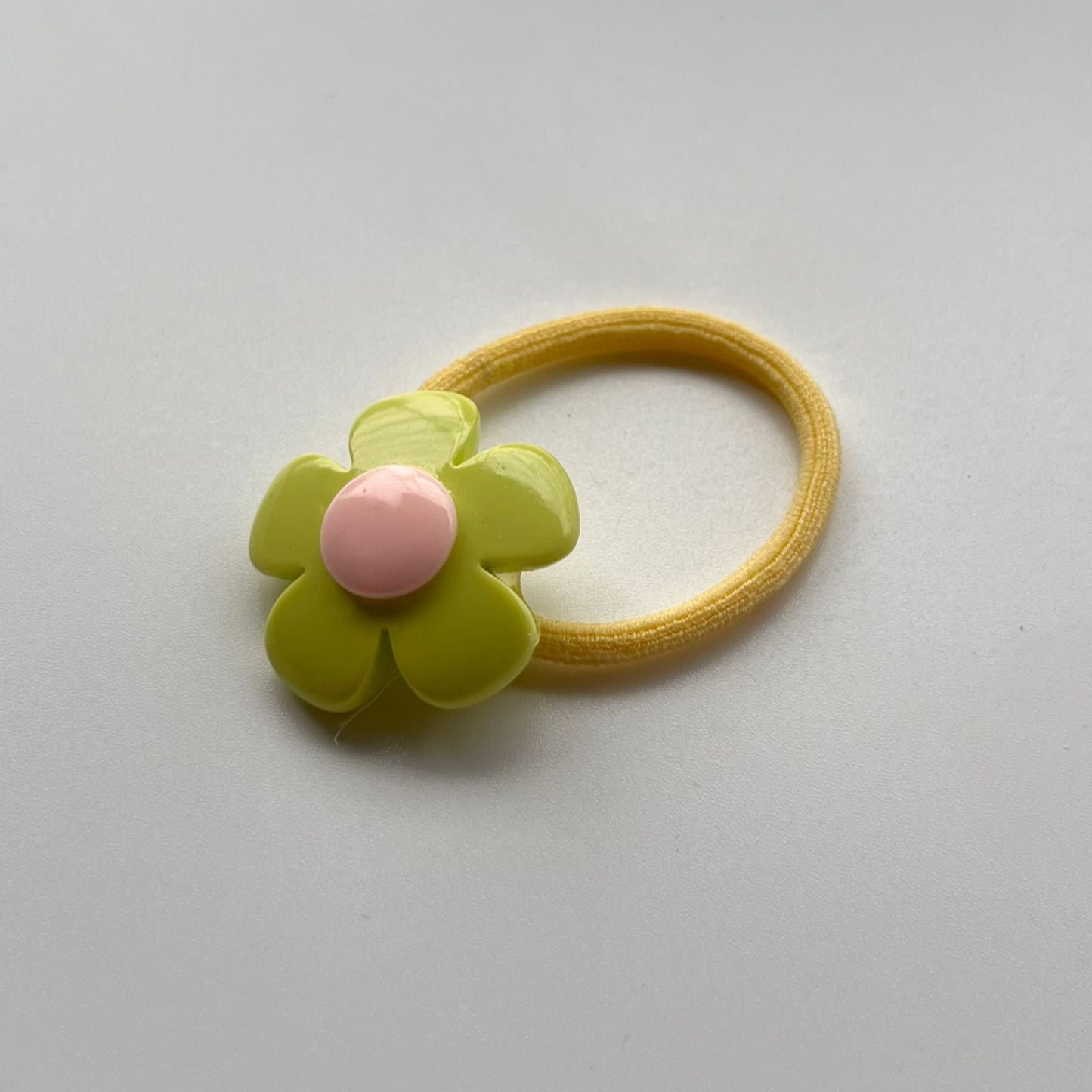 Yellow hair elastic with a green flower-shaped clip on a light gray background