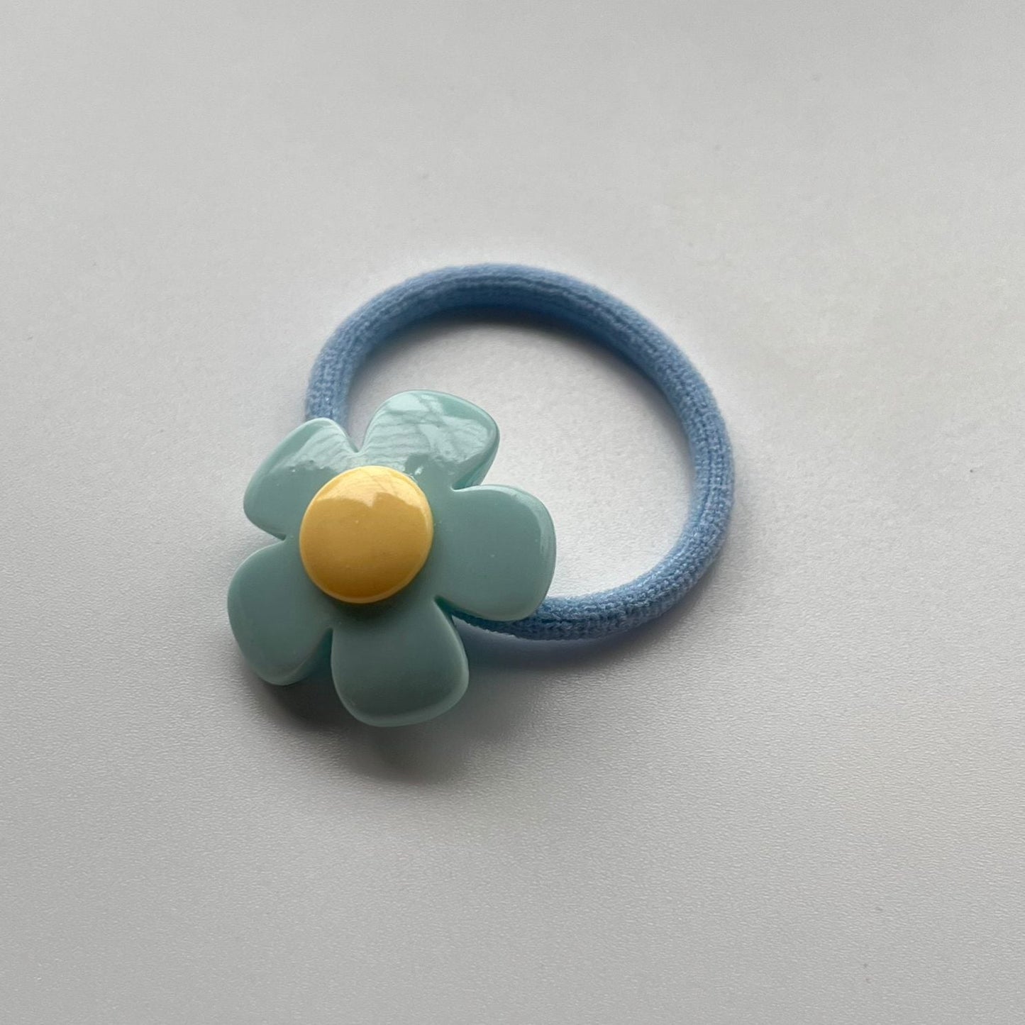 Blue hair elastic with a green flower-shaped clip on a light gray background