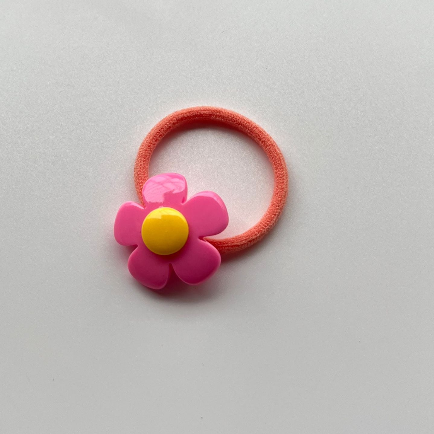 Pink hair elastic with a pink flower-shaped clip on a light gray background