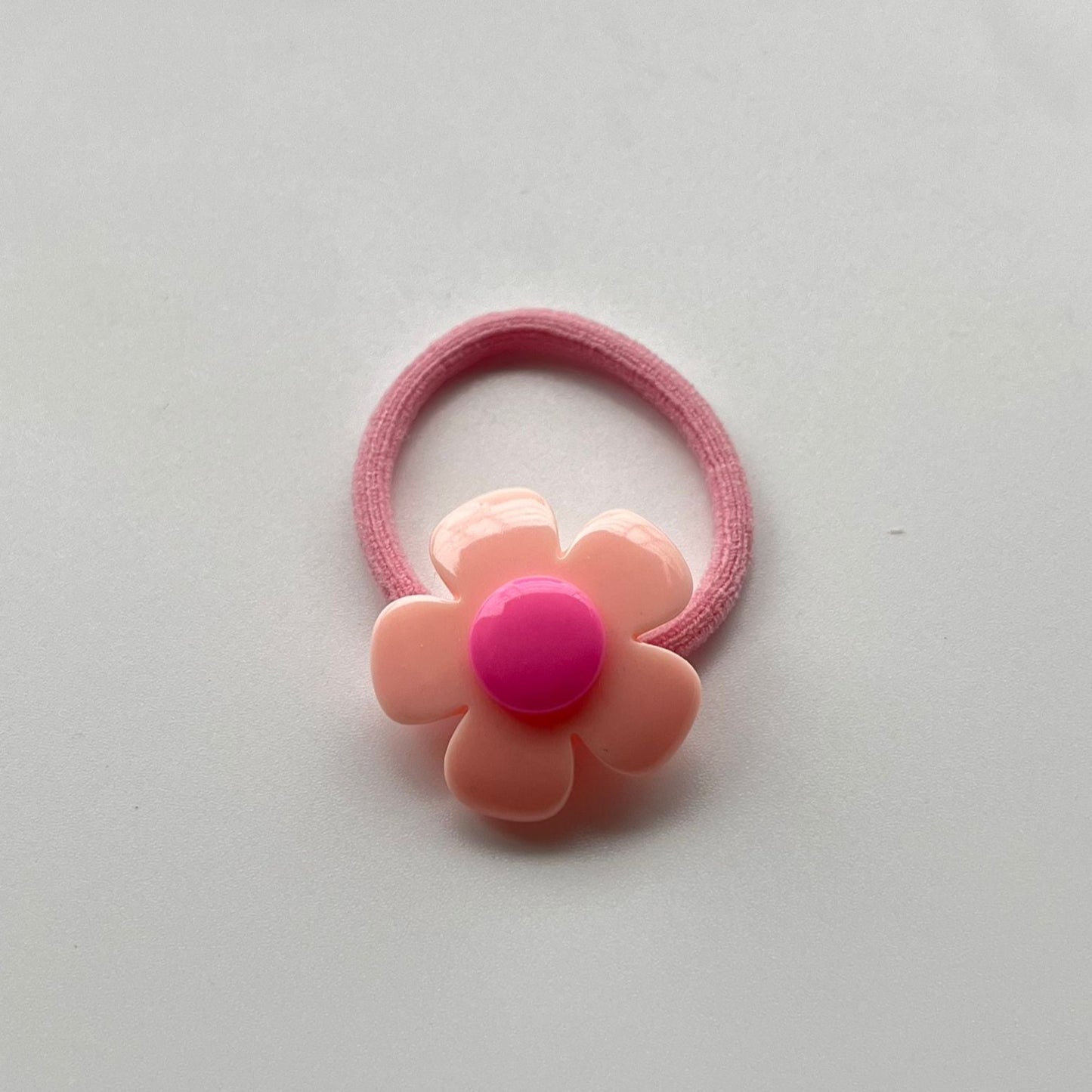 Pink flower-shaped hair tie on a light gray background