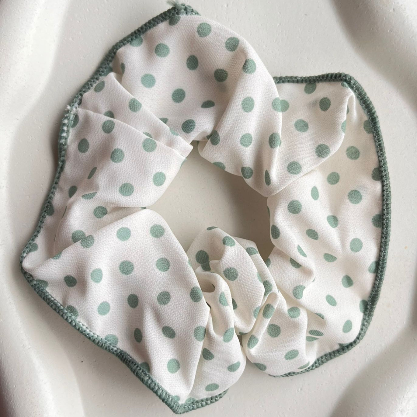 White scrunchie with green polka dots on a white background