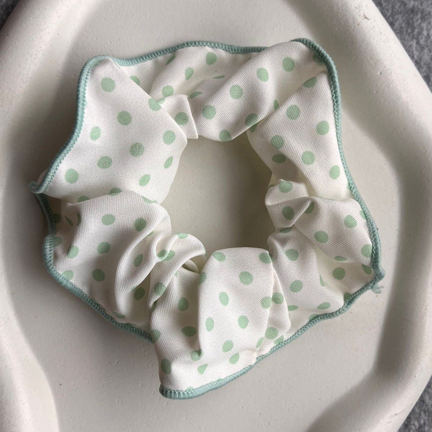 White scrunchie with green polka dots on a white ceramic dish