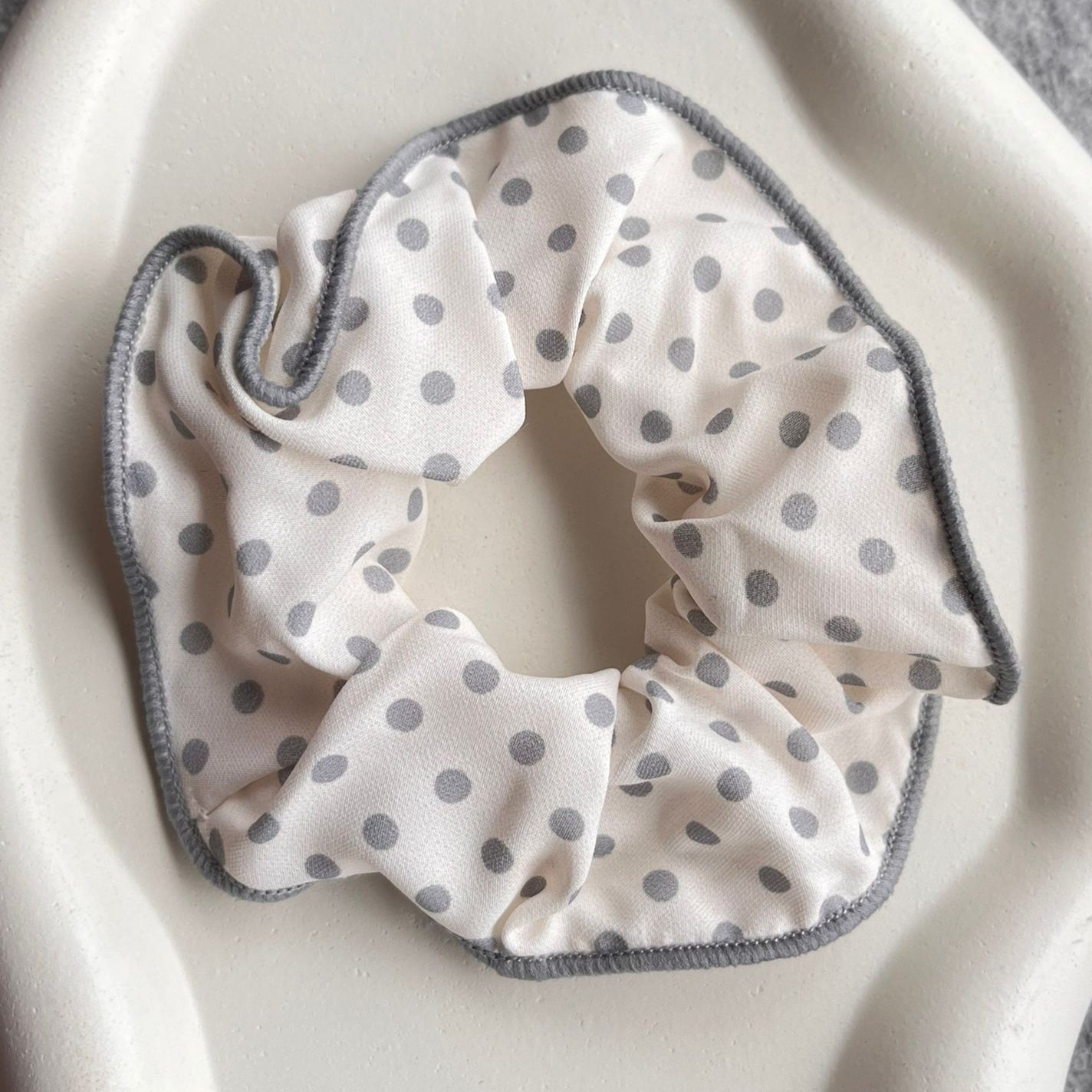 White scrunchie with gray polka dots on a white background