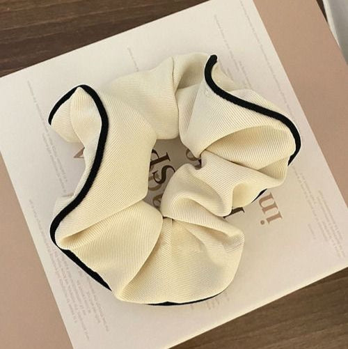 White or Cream scrunchie with black trim on a beige surface