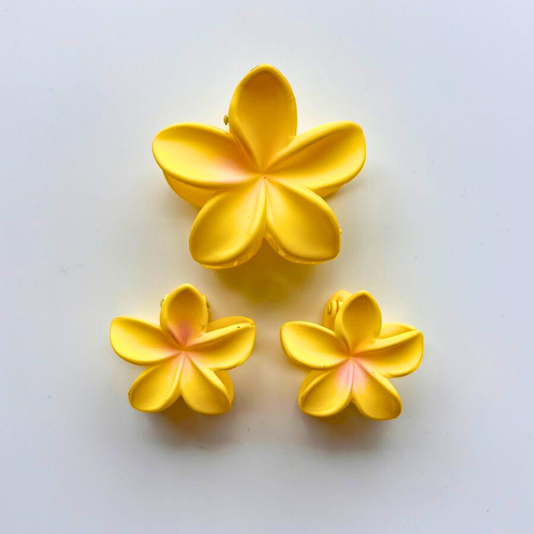 Three yellow flower-shaped claw clips on a white background.