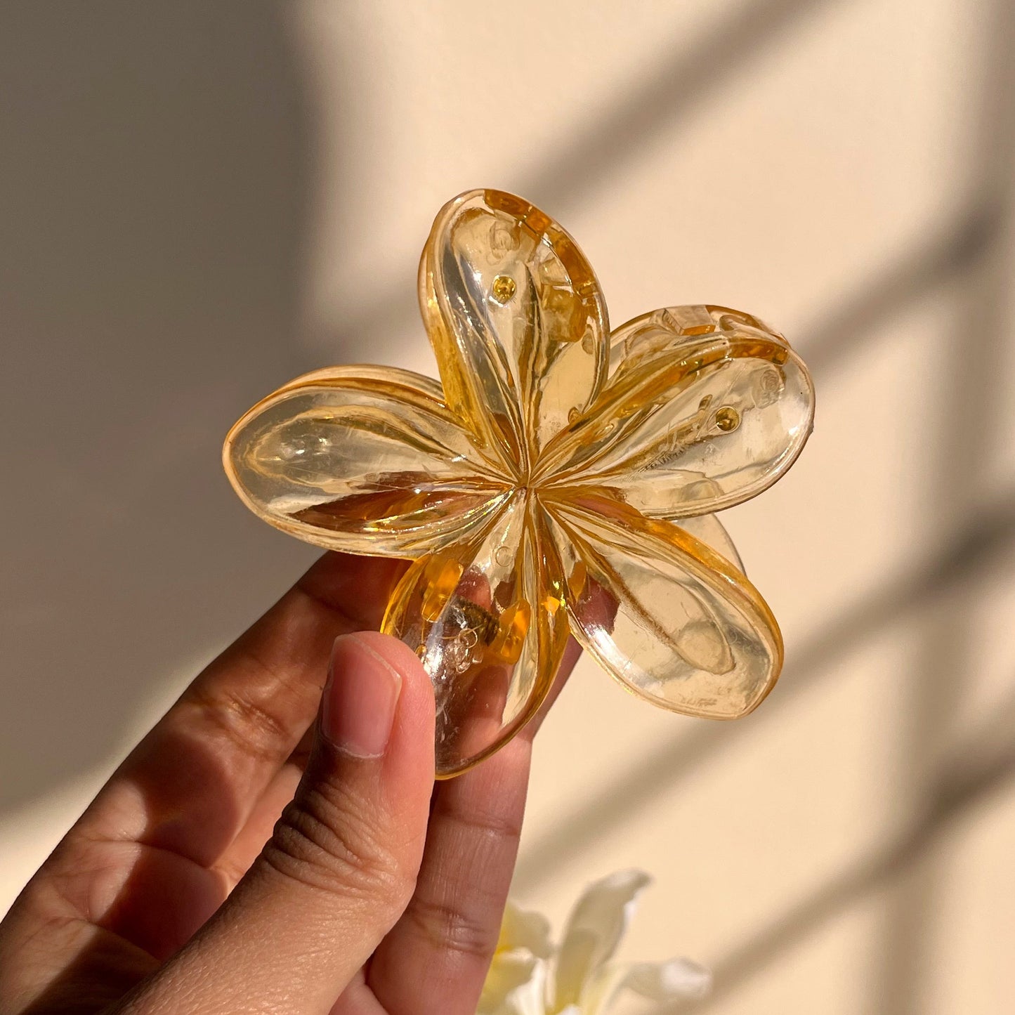 Hand holding a clear and gold flower-shaped object with white flowers in the background