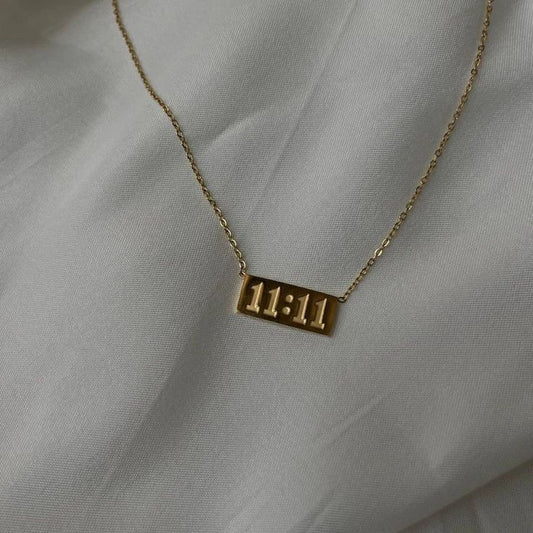Gold necklace with '11:11' pendant on a light gray fabric background